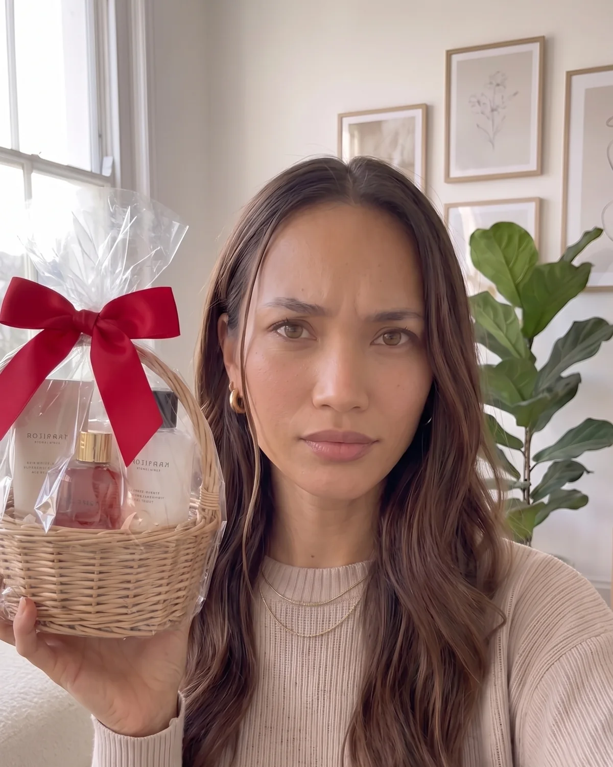 Mia Aquino looking unimpressed while holding up a wrapped gift basket of candles and toiletries